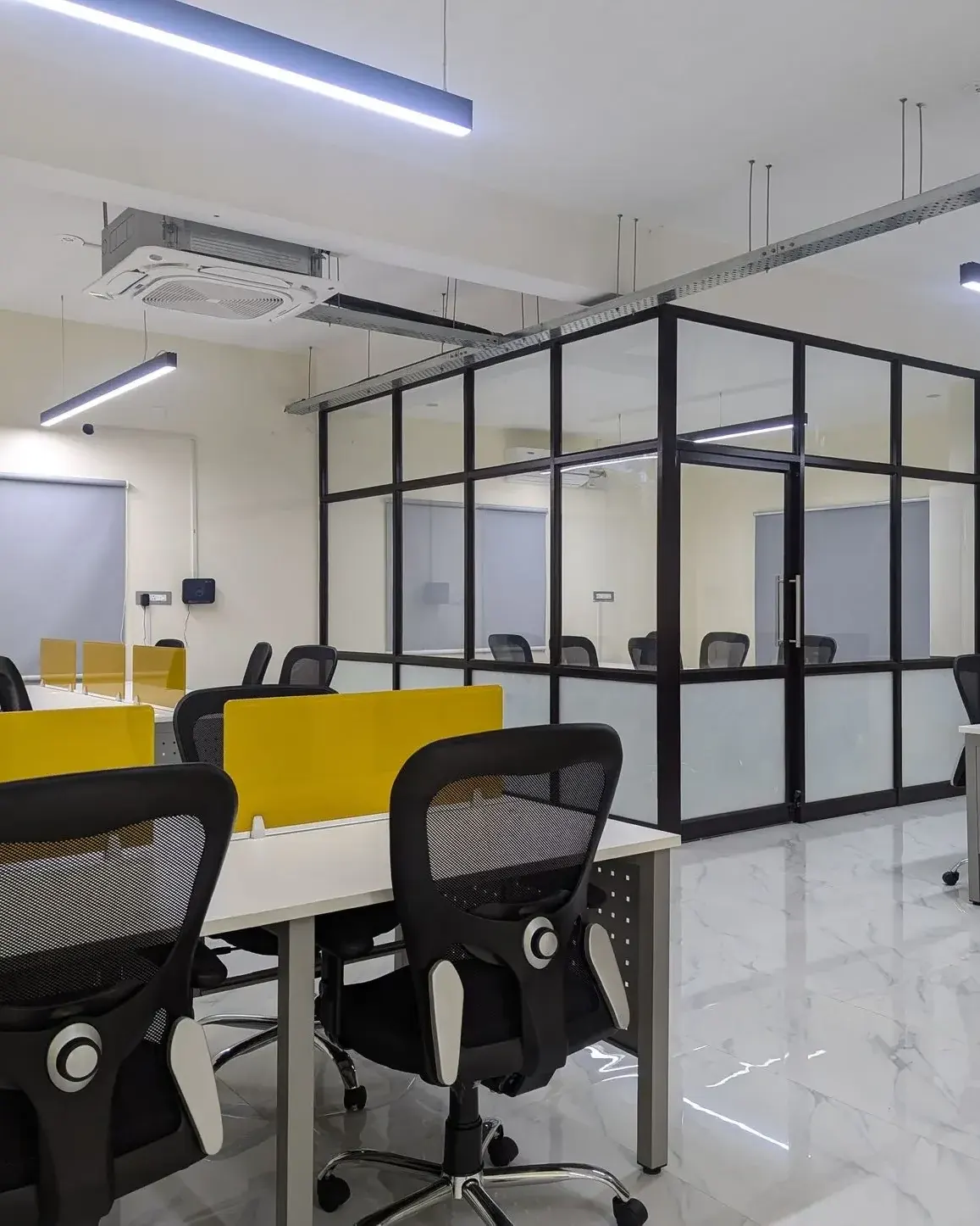 Open desks with yellow dividers and a glass meeting cabin inside Teapot Coworks coworking space, Woraiyur, Trichy